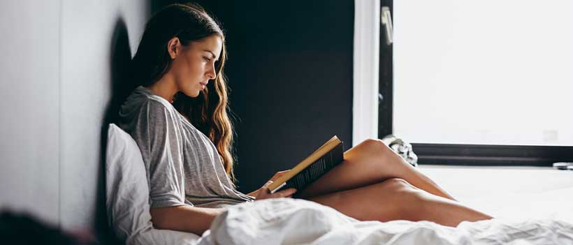 Junge Frau im Schlafzimmer liest ein Buch zur Weihnachtszeit