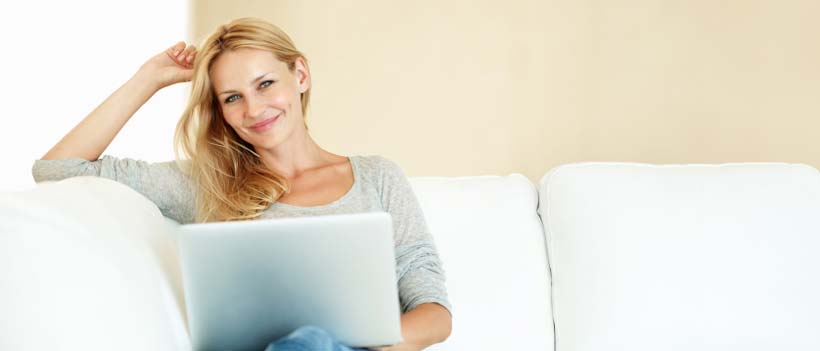 Porträt einer glücklichen Frau, die entspannt auf der Couch mit einem Laptop sitzt